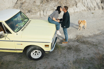 girl on truck hood kissing boy while dog looks on:vancouver wedding photographer