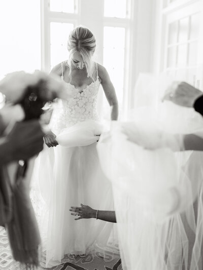 Black and white photo of bride holding one of the layers of her dress with hands holding her veil out off to the side