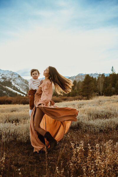 Mom is twirling while holding her baby boy in a field at  Palisades, Tahoe  City