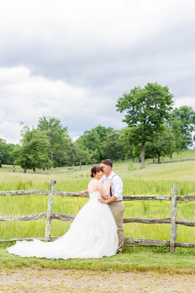 bride and groom standing close leaned on a fence in a pasture