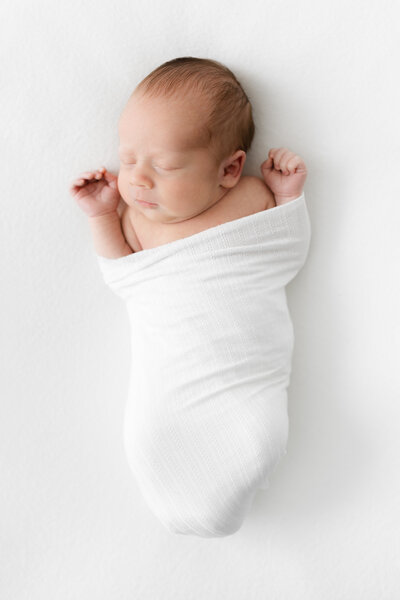 Newborn baby boy swaddled with his arms out of a white blanket by Washington DC Family PhotographerWashington DC Family Photographer