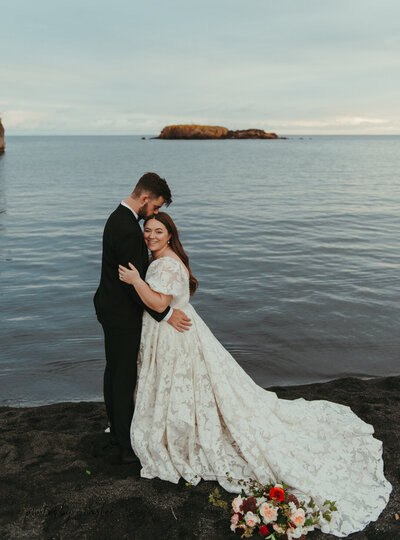 a bride and groom hugging on black sand beach