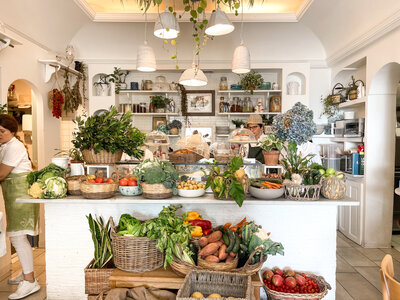 Interior shot of a room filled with counters and baskets full of fruits and vegetables and flowers