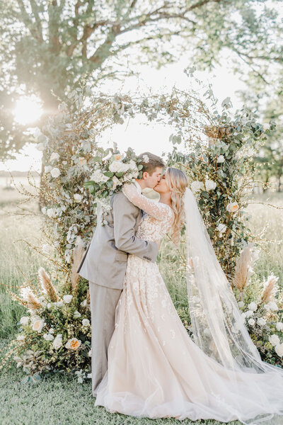 A gorgeous bride and groom kissing in front of a floral installation