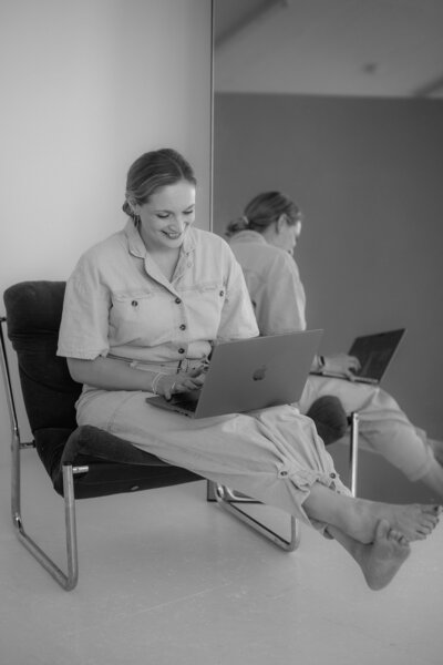 Karin Busch sitzt mit hochgelegten Beinen auf einem Sessel und arbeitet lächelnd an meinem Mac Book.
