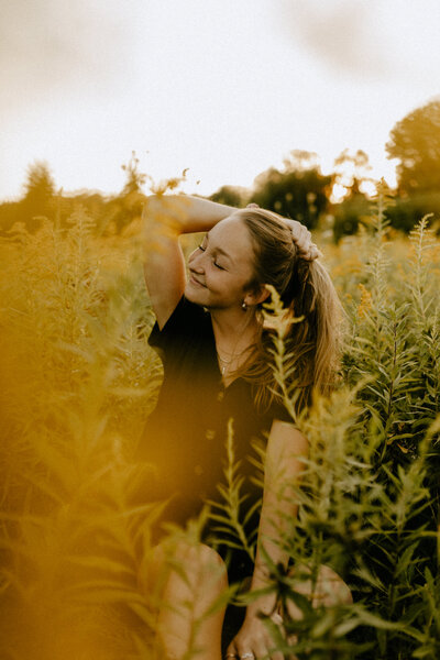 A girl sitting in a yellow field and smiling with her eyes closed