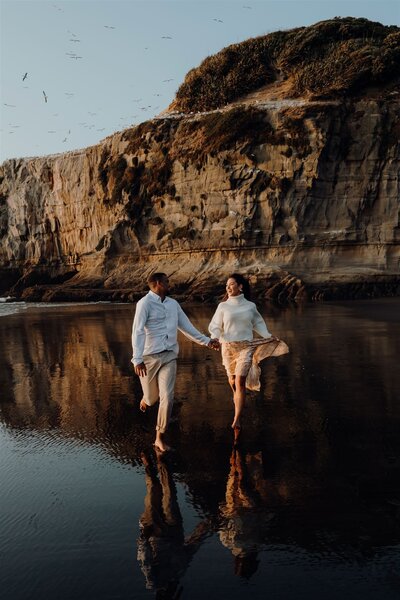 A couple running along the beach while being photographed during an engagement photoshoot with Haley Adele Photography