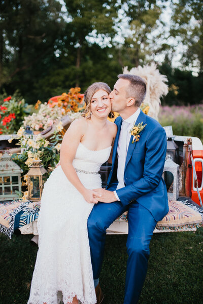 Groom kisses his bride's forehead while sitting in back of a pickup truck
