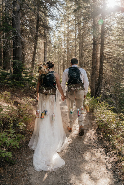 Montana Elopement Photographer. Couple holds hands while hiking in Glacier National Park with "just married" signs on their back packs.