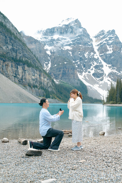 Man proposes to future wife on one knee at Moraine Lake in Banff National Park.