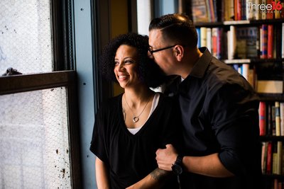 Groom to be whispers into his Bride's ear as she smiles and looks out the window at The Last Bookstore in LA