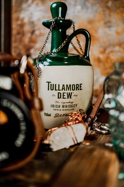 Discover the timeless charm of Tullamore Dew, the legendary triple-distilled Irish whiskey, in this evocative image. The classic 750ml ceramic jug bottle, established in 1829, is showcased alongside a vintage camera, epitomizing the legacy and craftsmanship of Irish spirits. Perfect for aficionados of fine whiskey and antique photography.