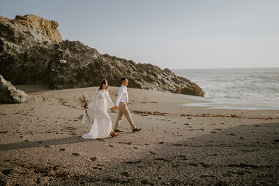 bride and groom holding hands walking on beach