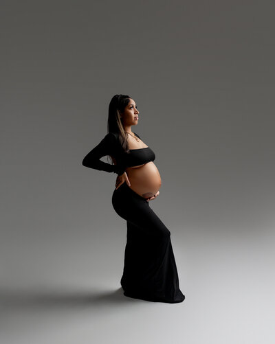 In a sleek black dress, she poses in profile, showcasing the elegance of her maternity glow. Captured by Inland Empire maternity photographer Kaitlyn Dawn Photography.