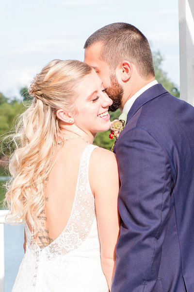 Groom whispers secret in his beautiful bride's ear as she smiles on their wedding day