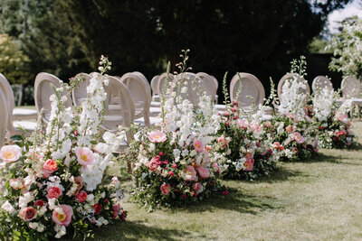 Elegant outdoor wedding aisle adorned with lush pink and white flowers, creating a romantic setting for an English garden wedding ceremony.