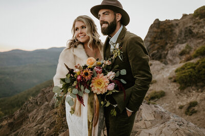 Bride in fur jacket and groom in green suit and hat near Skyliner Lodge in Bend Oregon