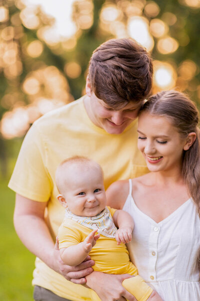Mom, dad, and baby boy hug and smile in a field