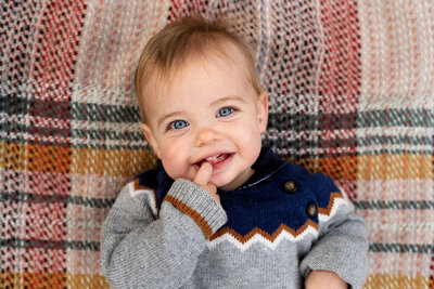 A young baby boy smiles into the camera while lying on a picnic rug during a family photo shoot