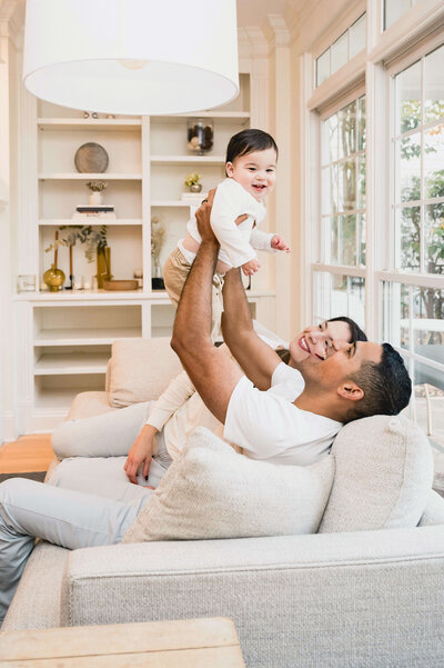 A father and mother holding their baby in the air in their Cary NC living room