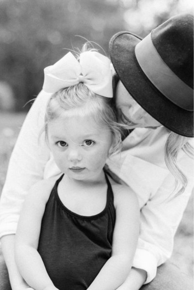 A little girl looks into  the  camera while sitting  on her moms lap  by New Orleans Family Photographer Casey McMurray