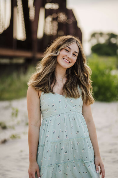 High School senior girl standing in the sand with a bridge running behind her