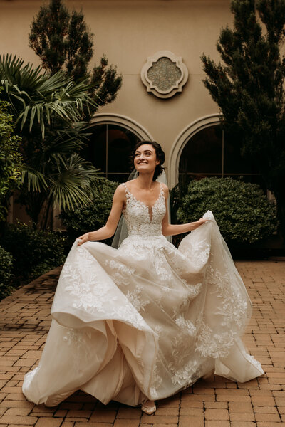 Bride steps through courtyard as she holds her bridal gown while smiling to the sky.