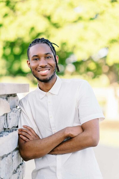 Teen guy wearing a white button up shirt and leaning against a stone wall