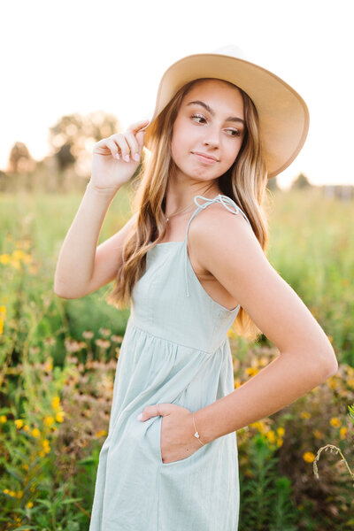 A high school senior with floppy hat and blue dress in flower field at sunset in Lexington KY senior photo session.