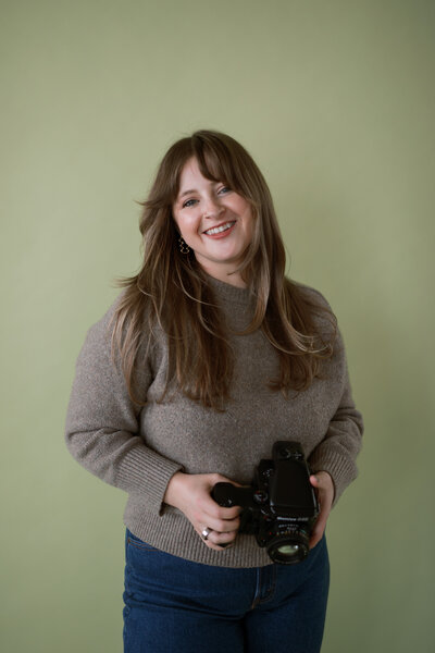 woman poses with hands in pockets and camera in her hands