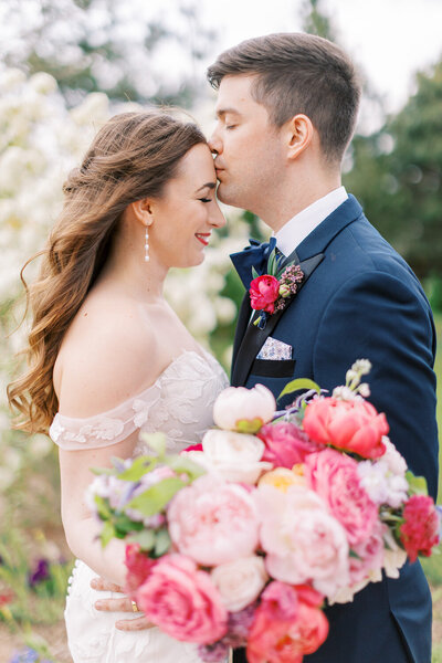 Groom kisses his bride on the head with a large pink bouquet