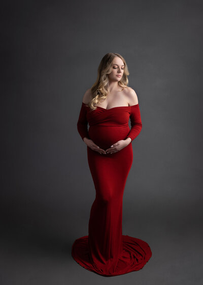 pregnangt woman in fitted red off the shoulder dress posing holding her belly