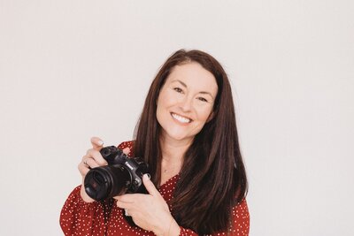 Kelli smiling while sitting on a bench and holding a camera