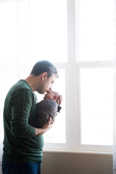 Dad holding and kissing his newborn son at an in-home photo session by Jamie Smith Photography
