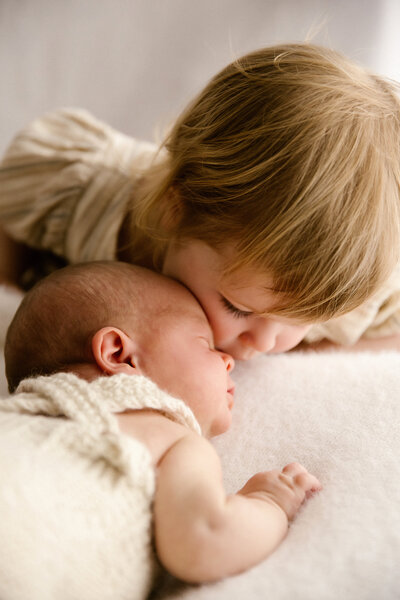 A baby being kissed by his sister in a newborn photoshoot pose in the studio in new plymouth