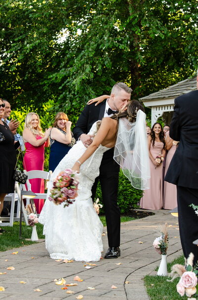Bride and groom sharing a celebratory dip kiss during an intimate outdoor wedding, photographed by Sarah Ferrazzani.