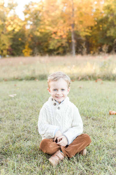 A photo of a sweet 5 year old boy sitting on the ground smiling at the camera by washington dc maternity photographer