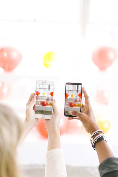 White hand holding a phone, brown hand holding a phone with identical images of red balloons