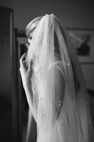 Bride adjusting her pearl-dotted veil for portrait.