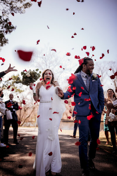 Couple walking down the aisle after exchanging vows with red rose petals in the air