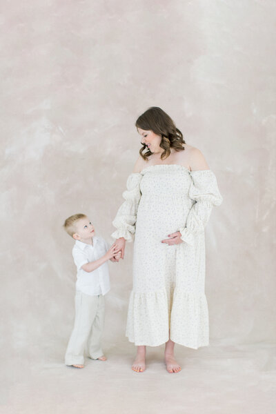 mom holds child's hand in front of painted backdrop at studio for maternity session