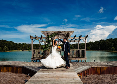 Groom twirls bride on a dock overlooking a lake at the Barn at Woodlake Meadows