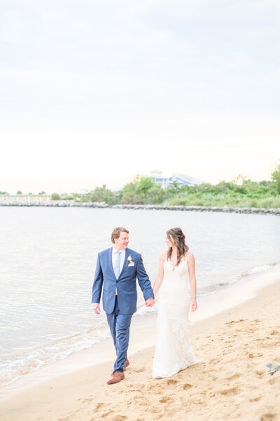 Bride and groom walk on the beach at Chesapeake Bay Beach Club during wedding day photographed by Wedding Photographer in Baltimore, MD