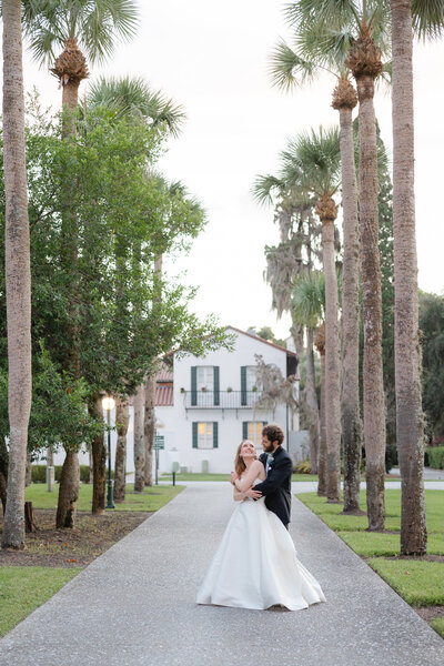 bride and groom snuggling on pathway lined with palm trees