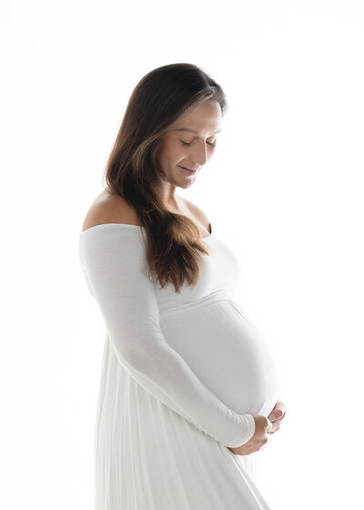 maternity client in form fitting white dress photographed in studio on a bright white background