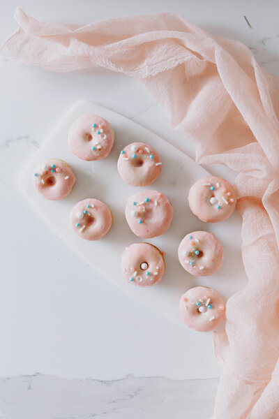 Light pink glazed mini cake donuts with pink, white, and blue sprinkles.