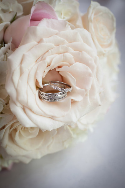 Silver edding bands inside a soft pink rose