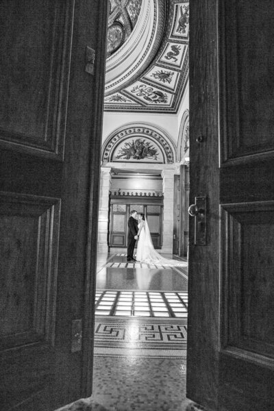 An open door show a bride  and groom  in a classy architecture.