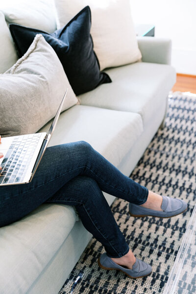 Woman working on her gold laptop while sitting on sofa with pillows
