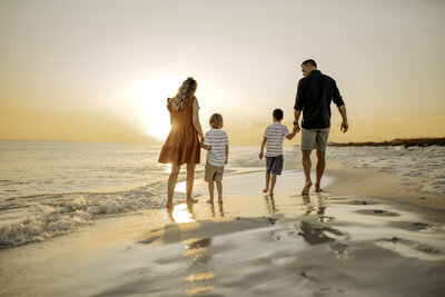 Family Photographer, a small family of four walk toward the quiet ocean waves at sunset